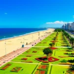 Panorama ensolarado da praia de Santos com jardins e prédios ao fundo.
