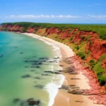 Vista aérea panorâmica da Praia de Pipa com falésias avermelhadas e mar verde-esmeralda.