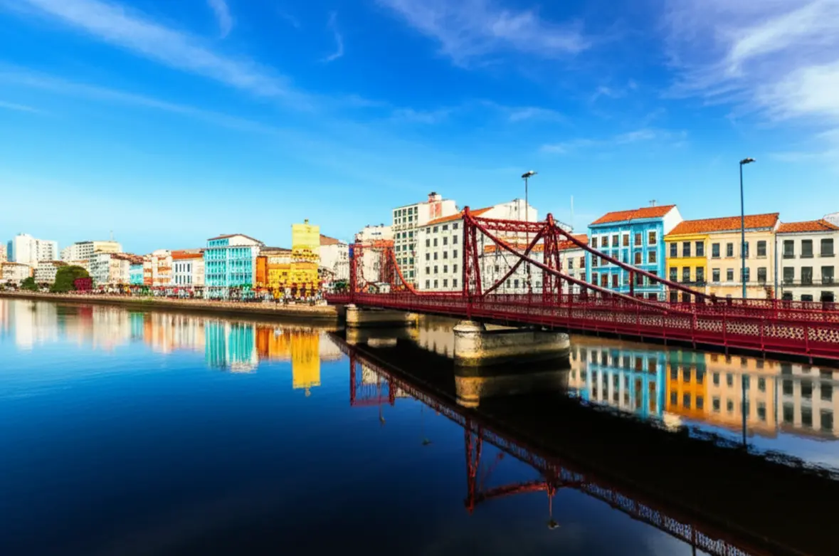 Fotografia de Recife com edifícios coloridos e pontes sobre o rio, sob o sol.