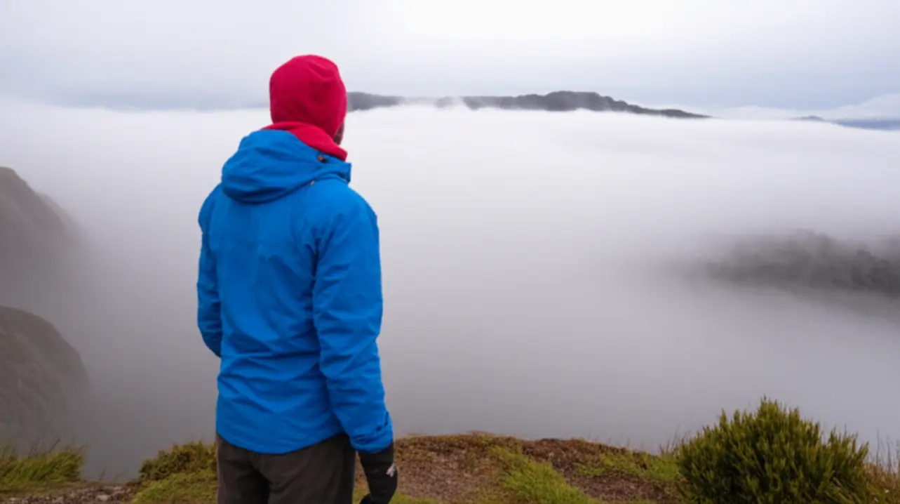 Pessoa com roupas de inverno em mirante de Urubici, observando a neblina invadir o vale.