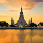 Vista panorâmica do templo Wat Arun refletido no rio Chao Phraya ao pôr do sol.