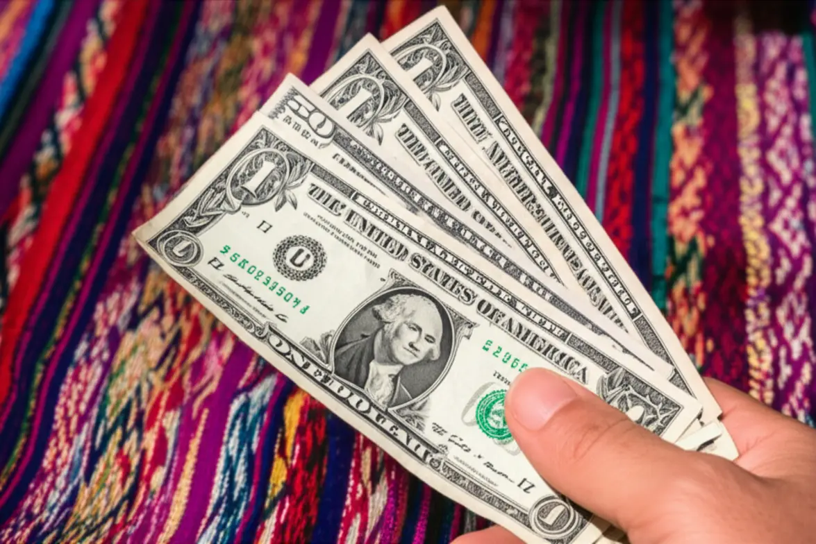 Mão segurando notas de dólares americanos em um mercado de artesanato em Quito.