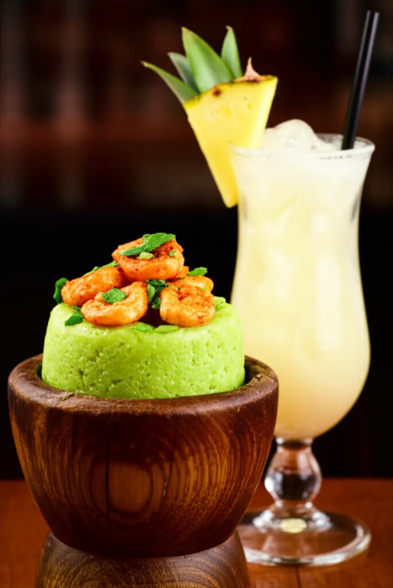 Prato tradicional de Mofongo com camarão ao lado de uma Piña Colada.