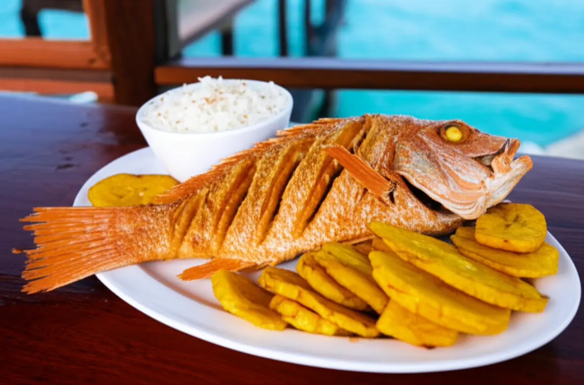 Prato de pargo vermelho frito com arroz de coco e patacones em mesa de madeira sobre o mar.