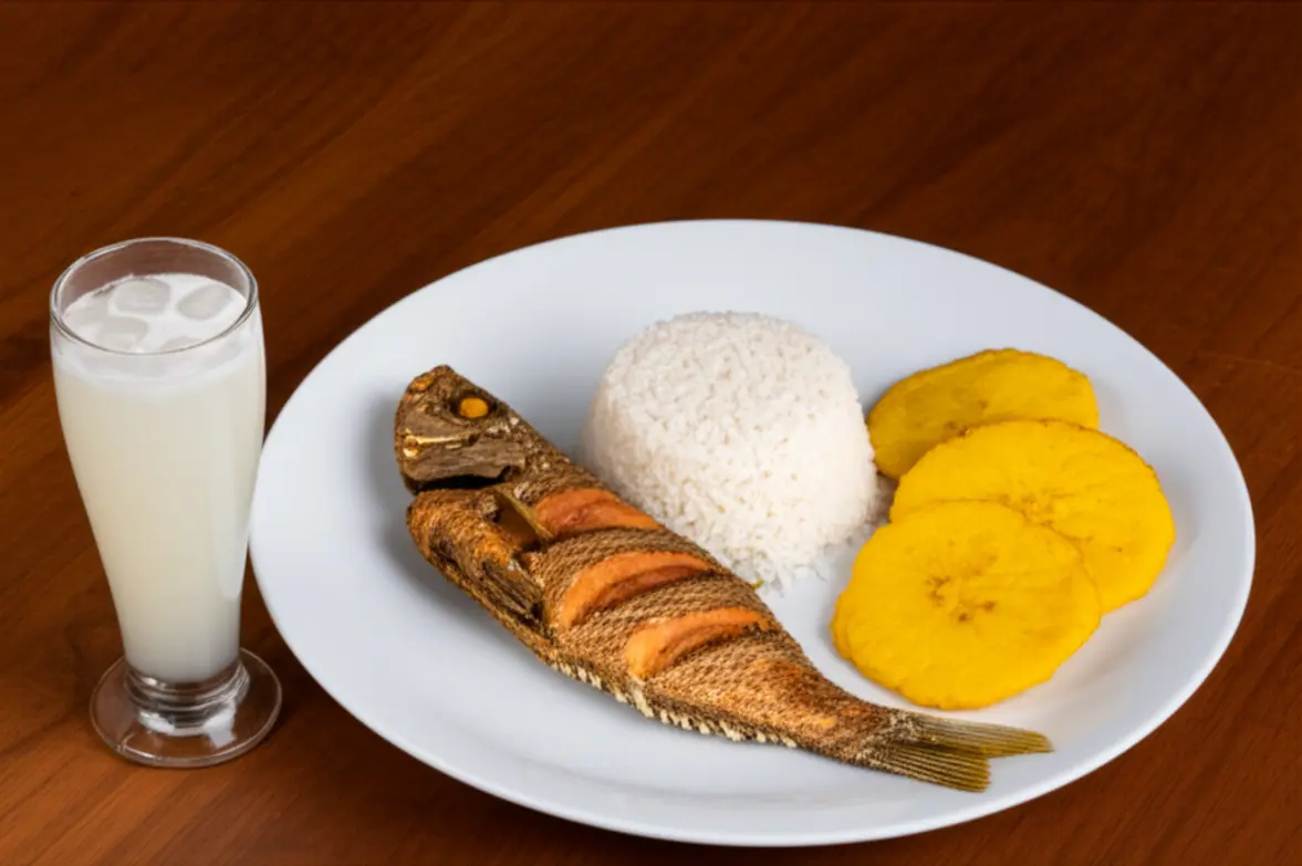 Prato típico de Cartagena com peixe frito, arroz de coco e patacones ao lado de uma limonada de coco.