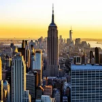 Vista panorâmica do skyline de Nova York com o Empire State Building sob um céu de pôr do sol alaranjado.