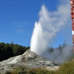 Gêiser Pohutu em erupção ao lado de esculturas tradicionais Maori em Rotorua.
