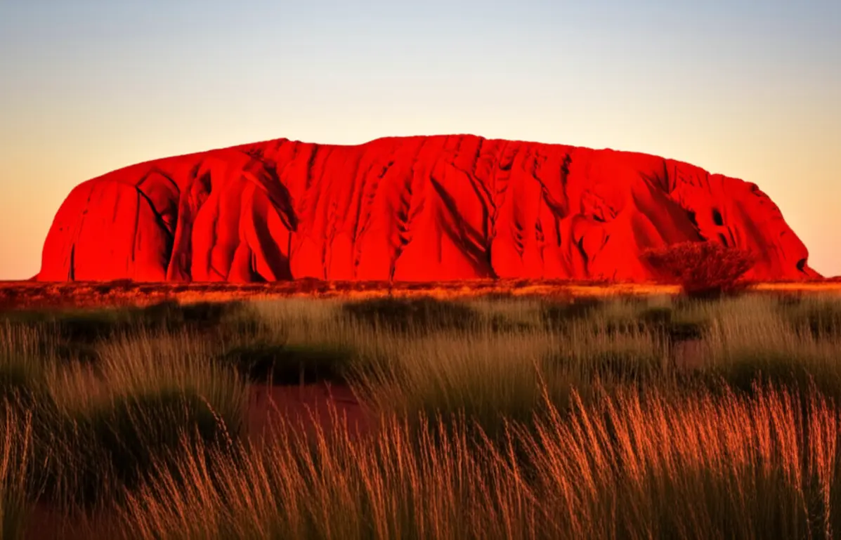 O monólito de Uluru brilhando em vermelho intenso durante o pôr do sol.