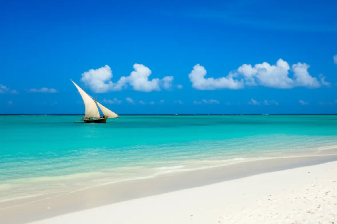 Praia paradisíaca em Zanzibar com areia branca e barco tradicional Dhow.