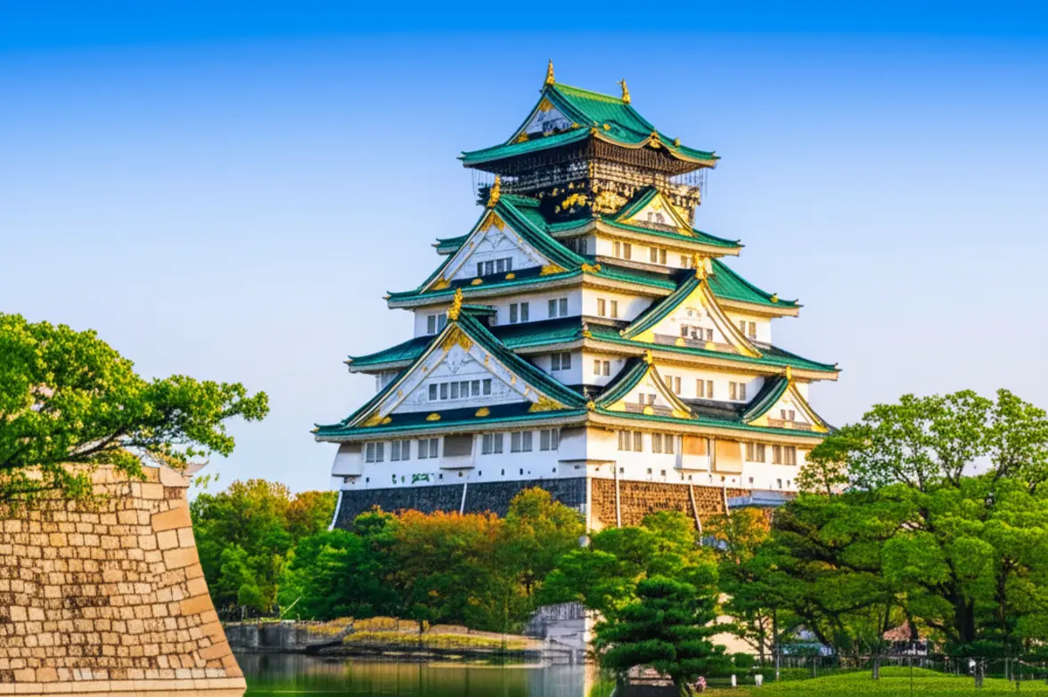 Vista majestosa do Castelo de Osaka cercado por árvores e muralhas históricas.