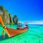 Barco tradicional tailandês em águas cristalinas de Phuket com falésias ao fundo.