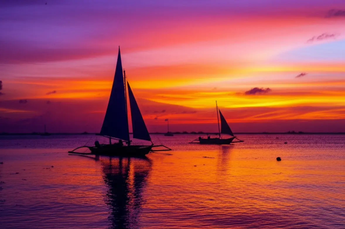 Pôr do sol vibrante em Boracay com silhuetas de veleiros Paraw no horizonte.