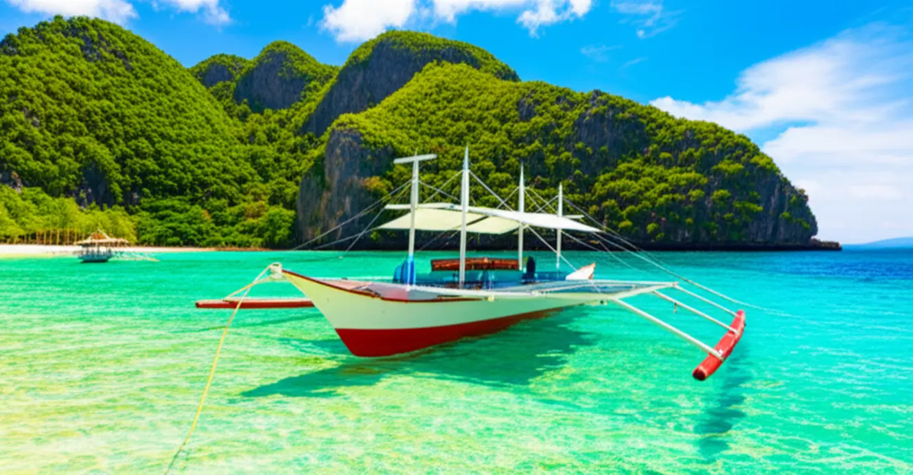 Barco tradicional filipino ancorado em águas cristalinas de Puka Shell Beach.