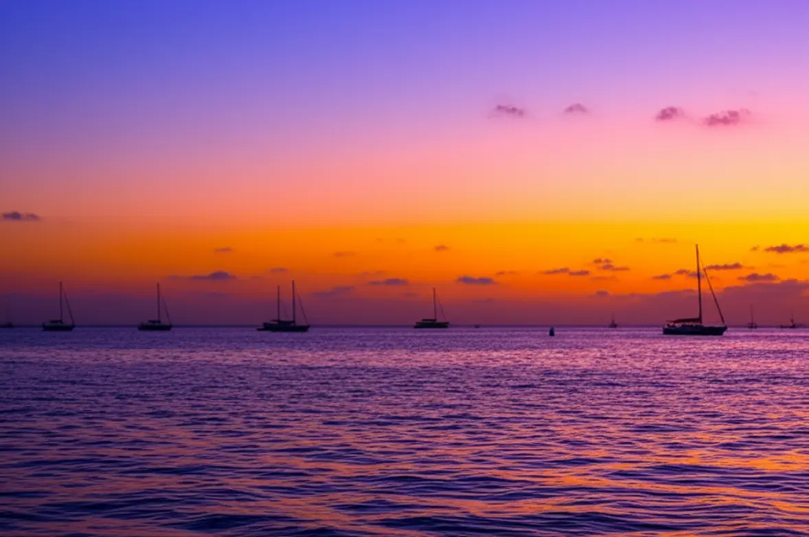 Pôr do sol vibrante na Mallory Square com silhuetas de barcos à vela.