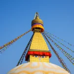 Estupa de Boudhanath em Catmandu com bandeiras de oração coloridas sob céu azul.