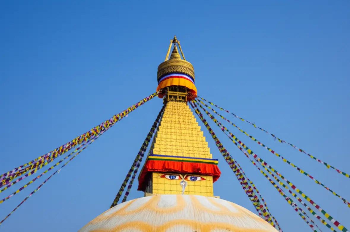 Estupa de Boudhanath em Catmandu com bandeiras de oração coloridas sob céu azul.