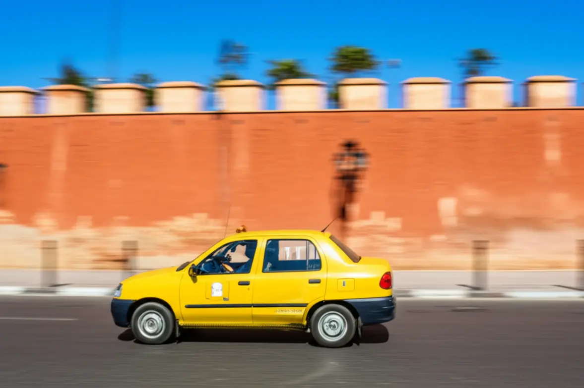Táxi amarelo típico de Marraquexe circulando perto das muralhas da cidade.